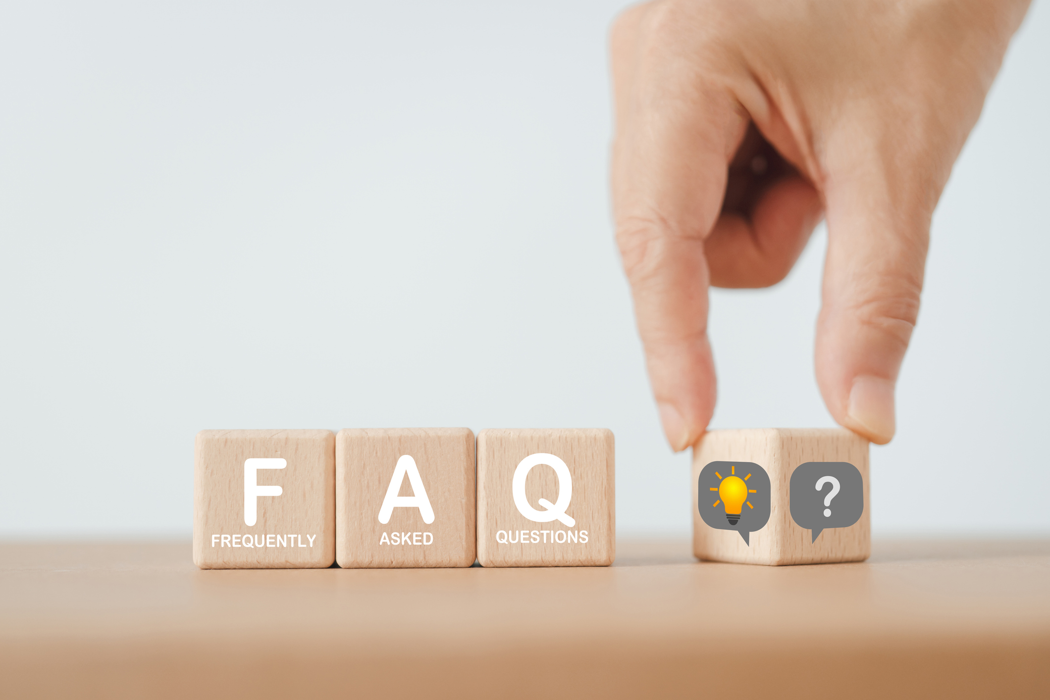 A plumber FAQ concept featuring frequently asked questions (FAQs) on various topics and their corresponding answers. The FAQs are displayed on wooden cube blocks, with a hand flipping a question to reveal a lightbulb.