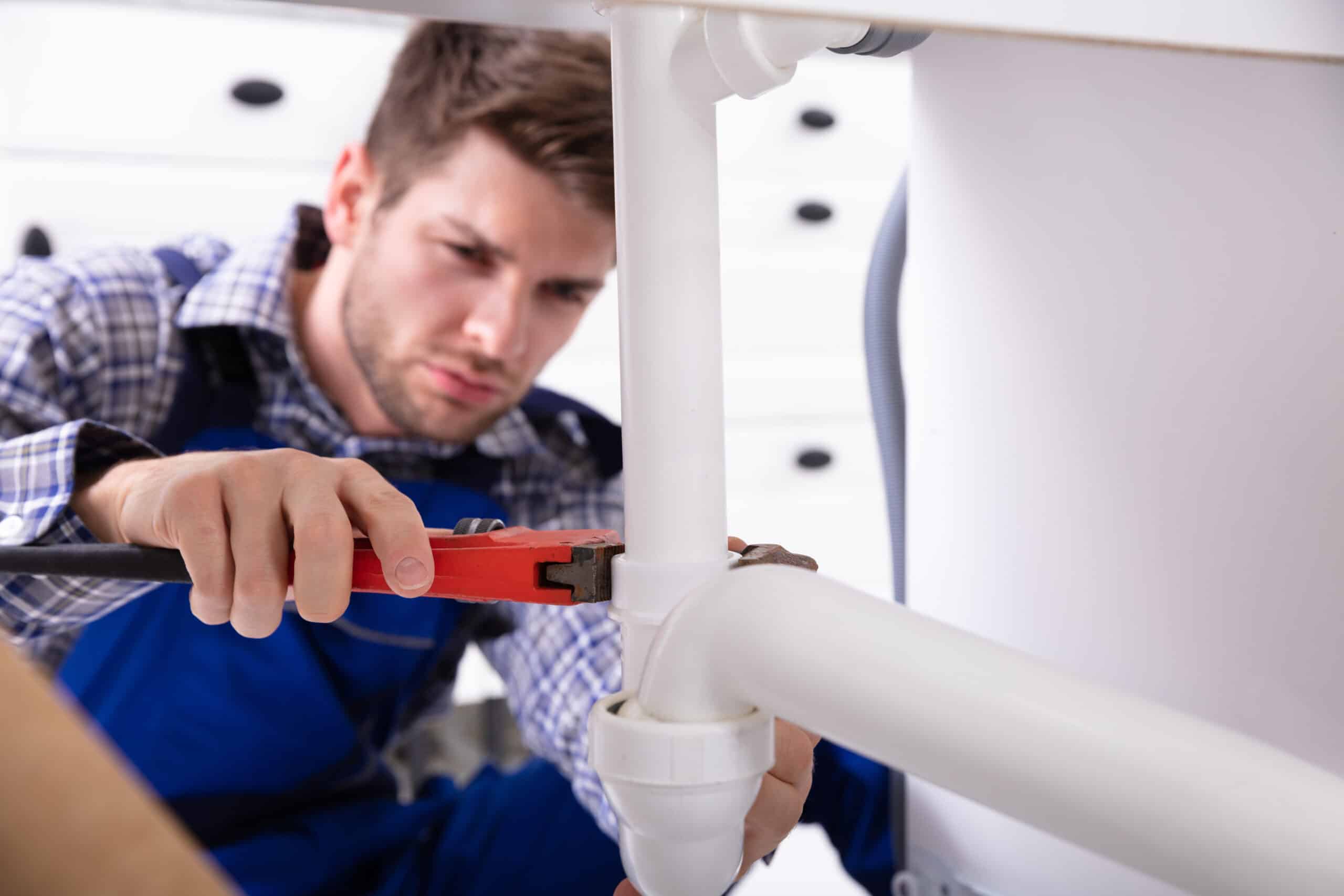 A plumber performing plumbing maintenance and repiping a sink pipe with an adjustable wrench.
